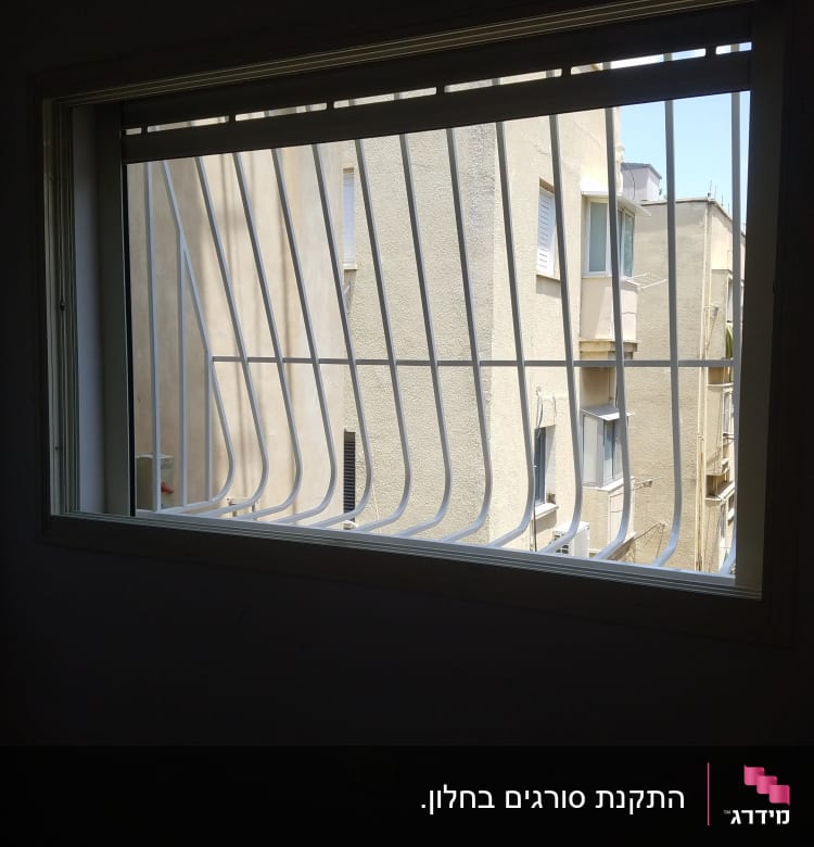 חלון עם סורגים מתכתיים מול בניין סמוך